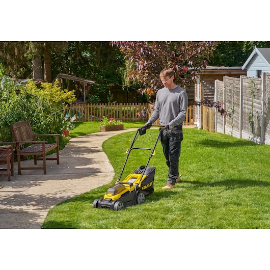 STANLEY SCMWP3401M1-XE lawn mower in use on grass in a garden setting, side angle.