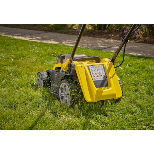 STANLEY SCMWP3401M1-XE lawn mower in yellow and black cutting grass, rear view, outdoors.