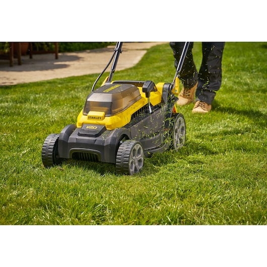 Photo of STANLEY SCMWP3401M1-XE lawn mower in use on green grass, with grass clippings visibly flying.