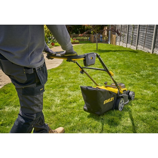 Photo of a person using a STANLEY SCMWP3401M1-XE lawn mower on green grass, rear angle view.
