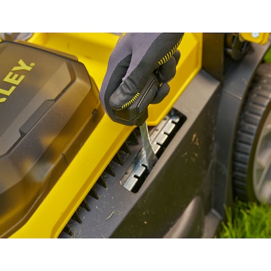 STANLEY SCMWP3401M1-XE lawn mower detail showing height adjustment lever and gloved hand on side view.