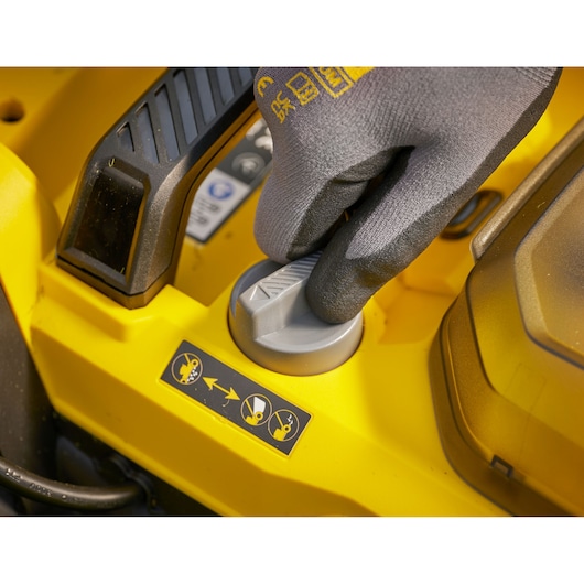 STANLEY SCMWP3401M1-XE lawn mower control knob close-up with gloved hand, yellow housing, top view.