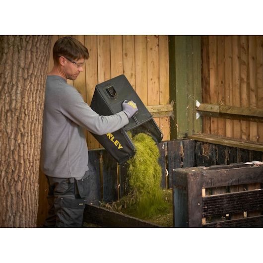 Photo of STANLEY SCMWP3401M1-XE lawn mower grass bag being emptied into a compost bin outdoors.