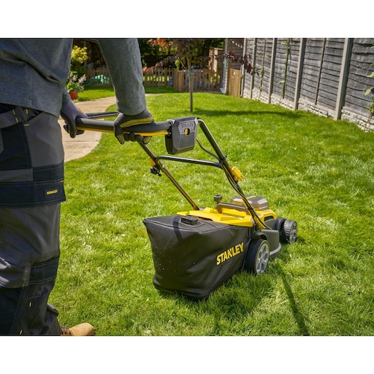 Photo of STANLEY SCMWP3701M2 lawn mower with black grass bag in use on green grass, rear angle.