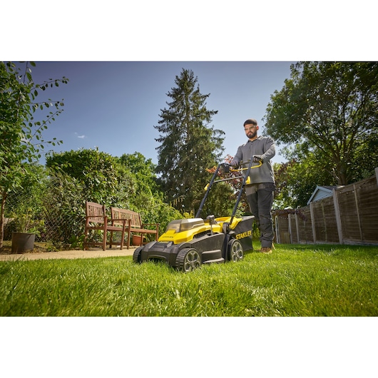 Photo of STANLEY SCMWP3701M2 lawn mower in use on grass in a garden setting, yellow and black design visible.