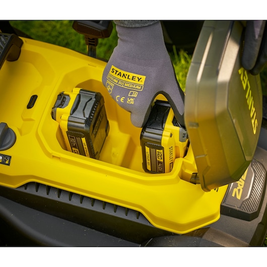 STANLEY SCMWP3701M2 lawn mower battery compartment with yellow batteries and gloved hand, top view.