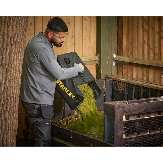 STANLEY SCMWP3701M2 lawn mower grass bag being emptied into wooden compost bin, outdoor photo.