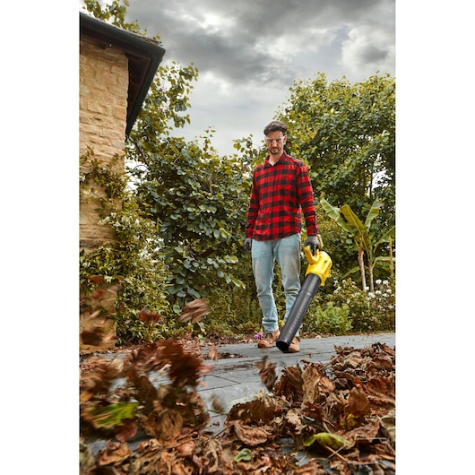 STANLEY SFMCBL7M1 leaf blower in use clearing leaves on garden path, yellow and black handheld tool.