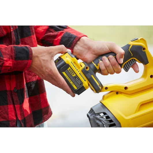 Photo of STANLEY SFMCBL7M1 lithium-ion battery being inserted into yellow power tool, close-up view.