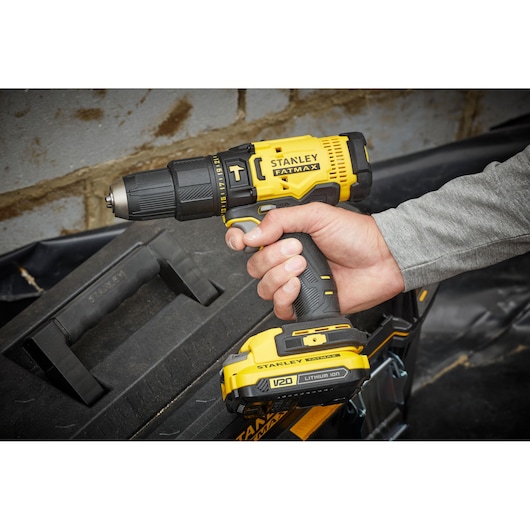 STANLEY SFMCD711D21 cordless drill, yellow and black, held in hand, side angle, tool box in background.