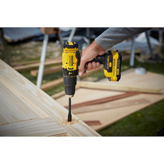STANLEY SFMCD711D21 cordless drill driving bit into wood, product held in hand outdoors.