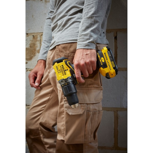 Photo of worker holding STANLEY SFMCD715D2K cordless drill, yellow and black, by side, close-up view.