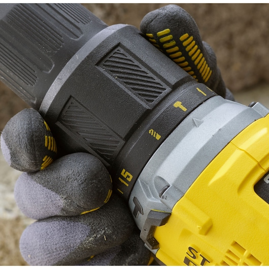 Photo of a gloved hand adjusting the torque settings on a STANLEY SFMCD715D2K cordless drill, close-up view.