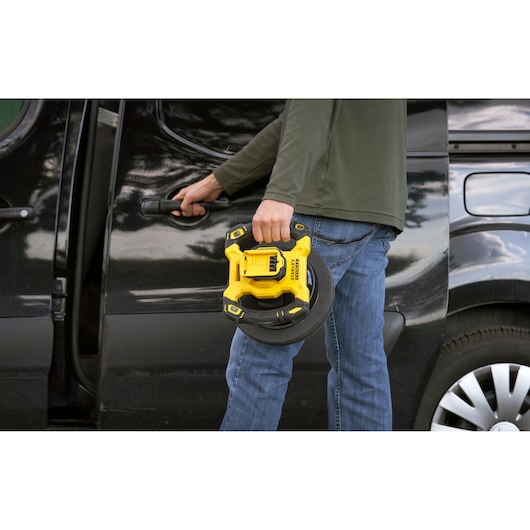 STANLEY SFMCE100D2 portable inflator held by person in front of black vehicle, outdoor setting.