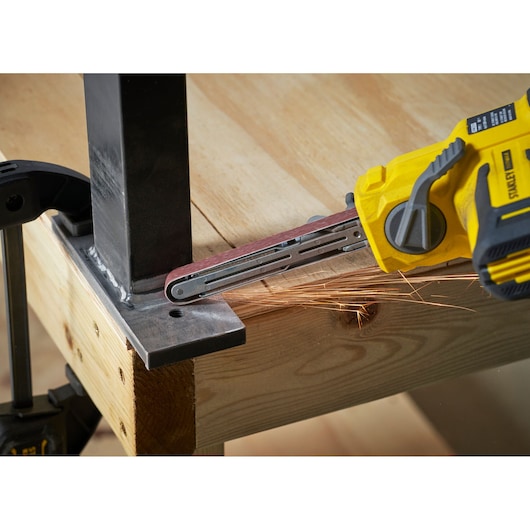 STANLEY SFMCE210B cordless belt file grinder sanding metal joint, close-up angle.
