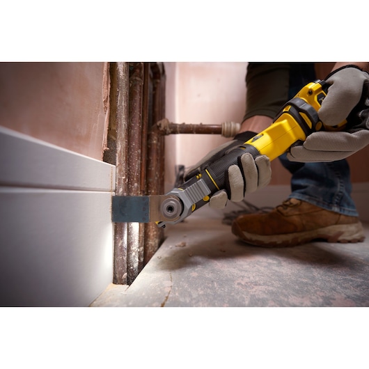 STANLEY SFMCE500B oscillating multi-tool in use, cutting trim near pipes, close-up action view.