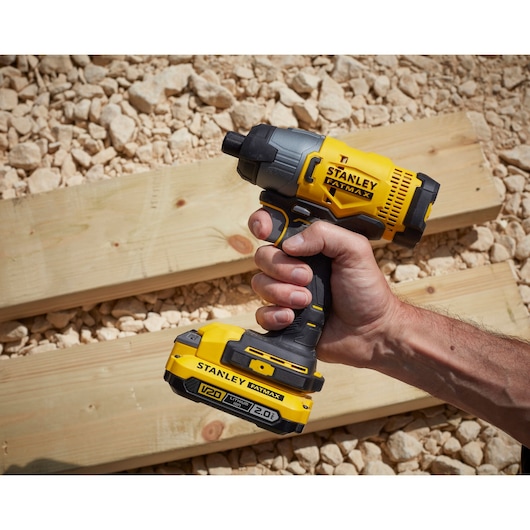 Photo of STANLEY SFMCF800D1K impact driver, yellow and black, held in hand on wood planks outdoors.