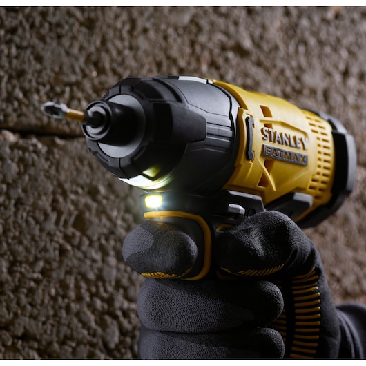 Stanley SFMCF800D1K impact driver held in gloved hand, close-up, yellow and black, drilling into masonry.