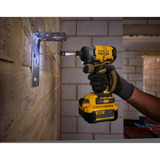 Stanley SFMCF810M1K impact driver drilling screw into metal bracket on brick wall, close-up view.