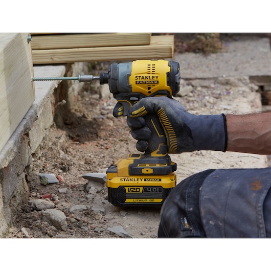 STANLEY SFMCF810M1K impact driver in use outdoors driving screw into wooden beam, construction setting.