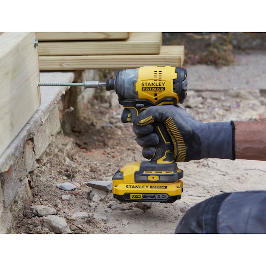 Photo of STANLEY SFMCF820D2K cordless impact driver in use, yellow and black design, driving screw into wood.