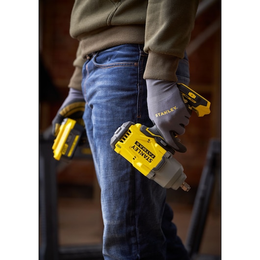 Photo of STANLEY SFMCF940B cordless impact wrench held by gloved person, focus on yellow and gray tool.