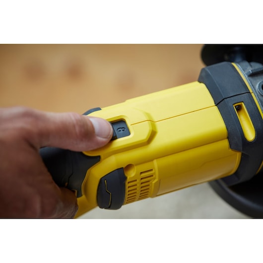 Photo of STANLEY SFMCG400B yellow cordless grinder close-up, hand pressing power switch.
