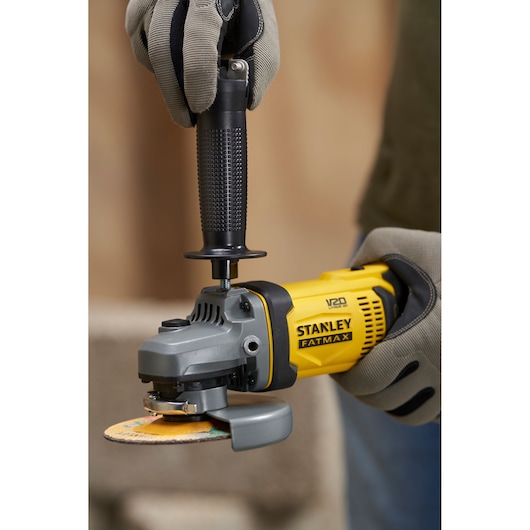 STANLEY SFMCG400D1K angle grinder in use, close-up of yellow and black tool held with gloved hands.