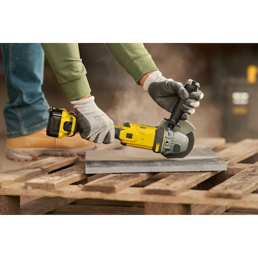 STANLEY SFMCG400M1K angle grinder in use cutting tile, yellow and black tool on wooden pallet outdoors.