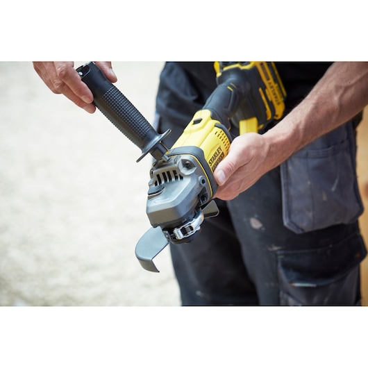 Photo of STANLEY SFMCG400M1K cordless angle grinder being held with black and yellow handle, side view.