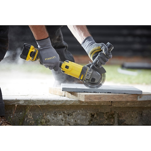 Photo of STANLEY SFMCG400M1K cordless angle grinder in use cutting a stone slab outdoors