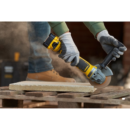STANLEY SFMCG700M2K angle grinder in use cutting stone, close-up photo of worker hands with gloves.