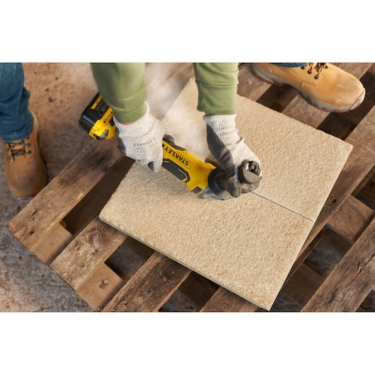 STANLEY SFMCG700M2K angle grinder cutting stone tile on wooden pallet, close-up photography.