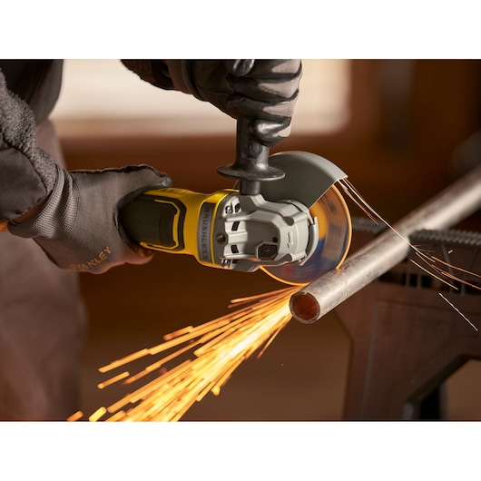 Stanley SFMCG700M2K grinder cutting metal pipe with sparks, close-up action shot.