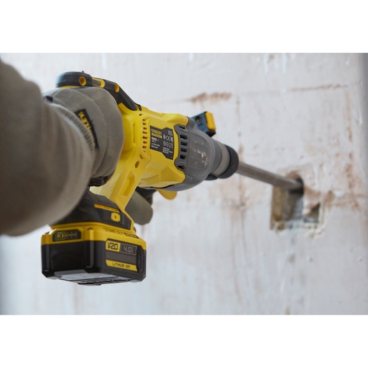 STANLEY SFMCH900M12 rotary hammer drill in use on wall, yellow and black, close-up side angle.