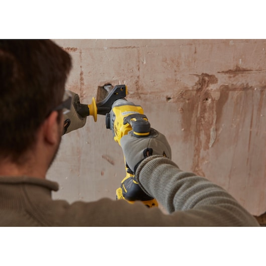 STANLEY SFMCH900M12 reciprocating saw in use against a plaster wall, close-up from behind.
