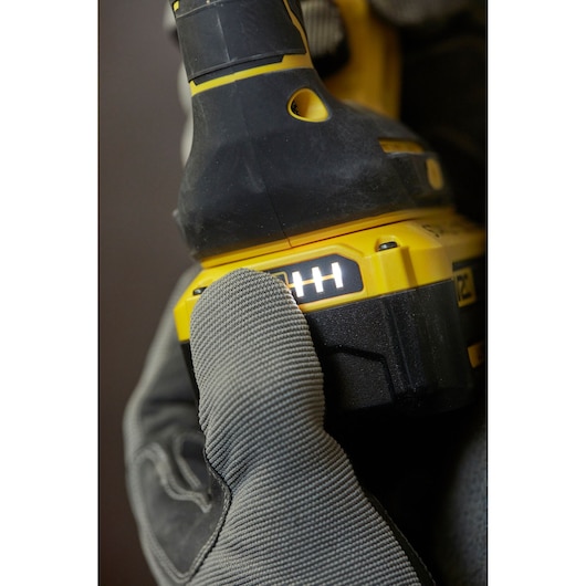 Photo of STANLEY SFMCH900M12 cordless drill battery indicator close-up, gloved hand pressing indicator button.
