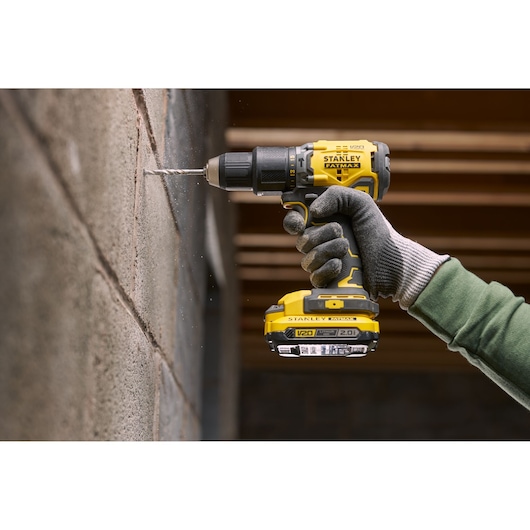 Photo of STANLEY SFMCK461D2S cordless drill in use drilling into a concrete wall, close-up of tool and gloved hand.