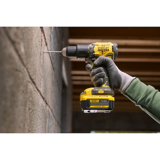 Stanley SFMCK461M2S cordless drill in use on a concrete wall, close-up side view, worker wearing gloves.
