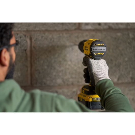 STANLEY SFMCK461M2S brushless cordless drill in use, shown close up drilling into concrete wall.