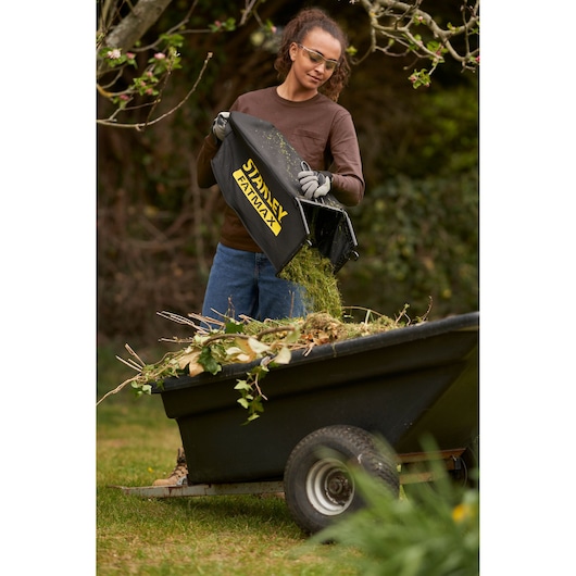 Photo of STANLEY SFMCMW2651M lawn mower grass bag being emptied into a garden trailer outdoors.