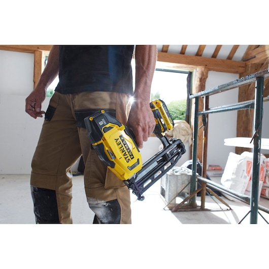 Photo of STANLEY SFMCN616B cordless nailer held by a worker in construction setting.