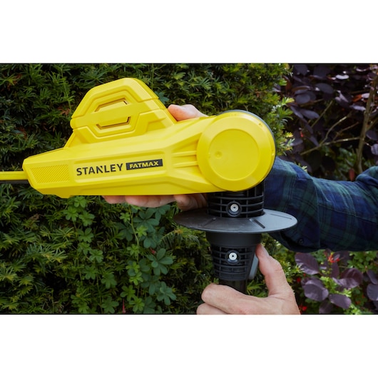 STANLEY SFMCPH845M1 yellow cordless hedge trimmer in use, close-up of handle and body with garden background.