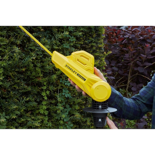 STANLEY SFMCPH845M1 hedge trimmer in use outdoors, yellow body with visible blade cutting green shrub.
