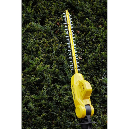 STANLEY SFMCPH845M1 hedge trimmer in use, yellow body with black accents, trimming green hedge.