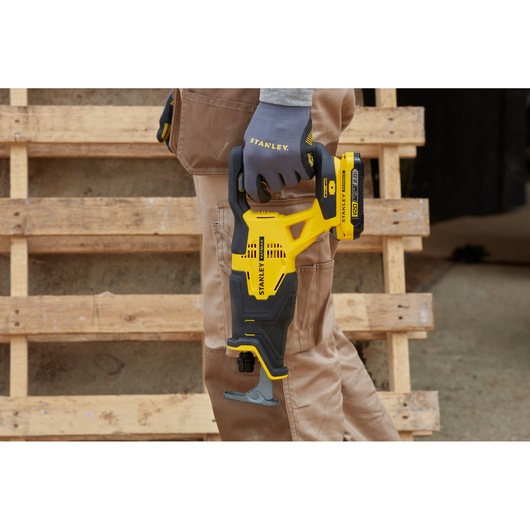 Stanley SFMCS300D1K yellow and black reciprocating saw held by gloved hand, shown outdoors near wooden pallets.