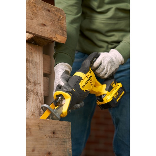 STANLEY SFMCS300M1K cordless reciprocating saw in use cutting wooden plank, close-up with worker hands.