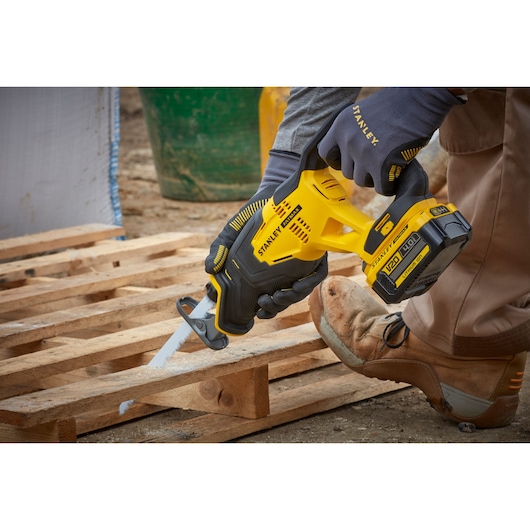 STANLEY SFMCS300M1K reciprocating saw in use, yellow and black, cutting wood pallet outdoors.