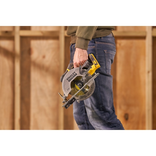 Photo of STANLEY SFMCS500D1K circular saw held by person in jeans, yellow and gray tool in workshop setting.