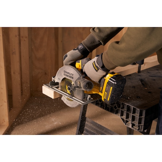 Photo of STANLEY SFMCS500M1K circular saw cutting wood, user wearing gloves, construction site background.